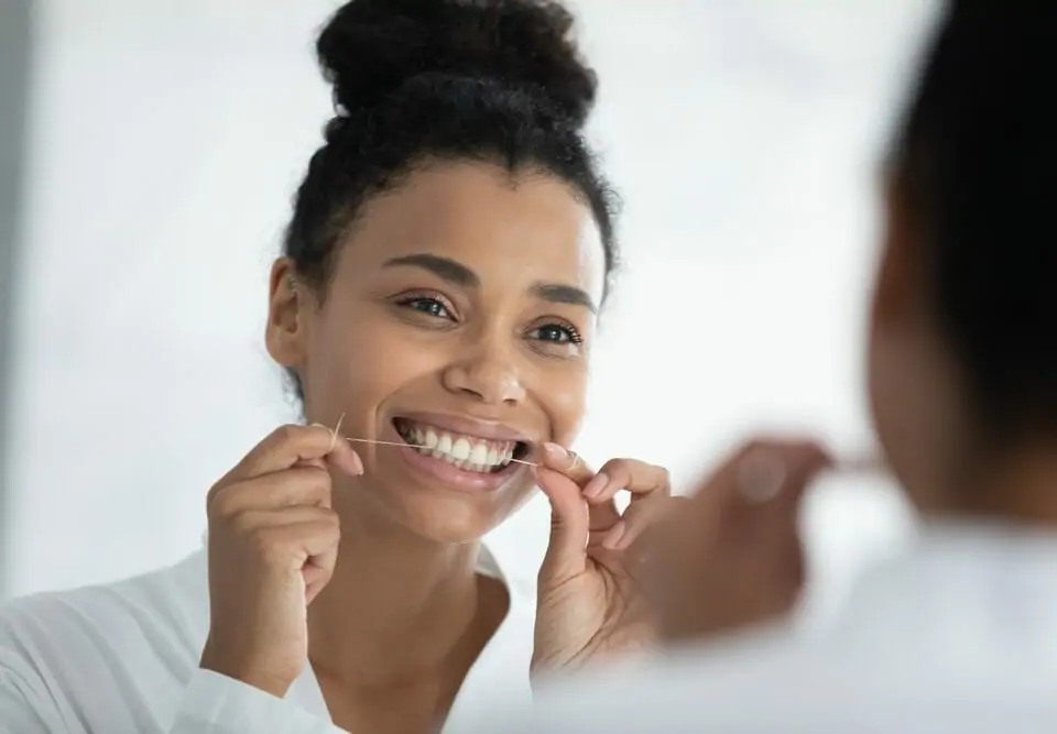 woman flossing her teeth in the mirror