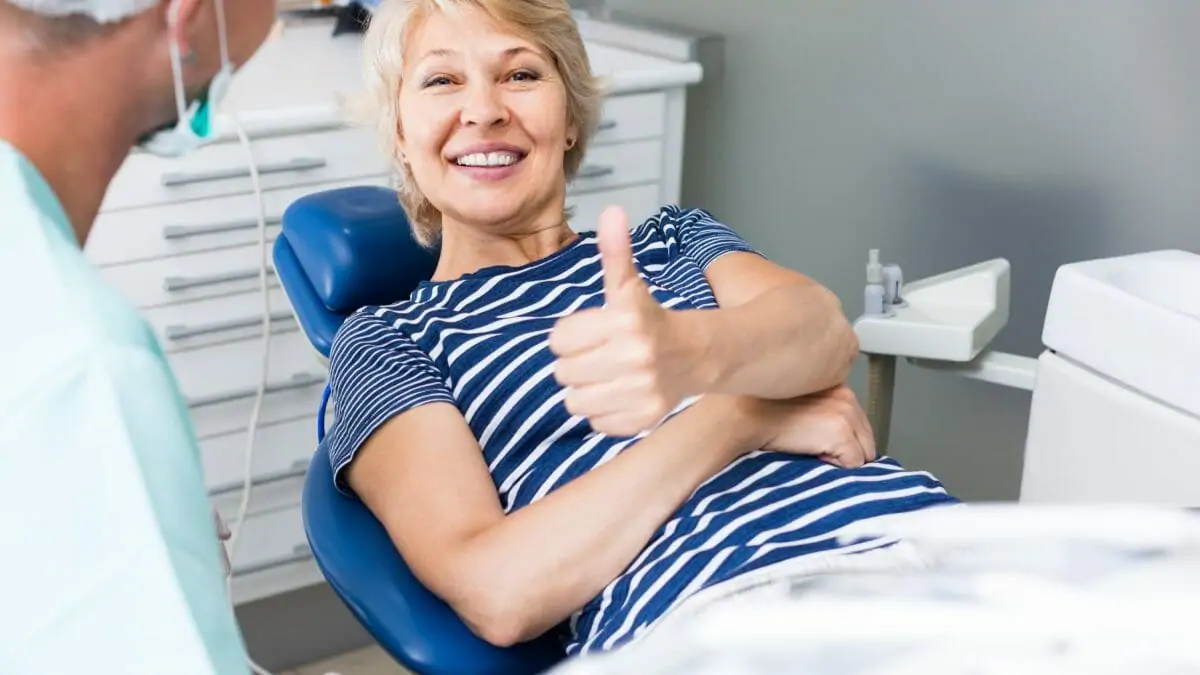 happy woman in dentist chair smiling with her thumb up