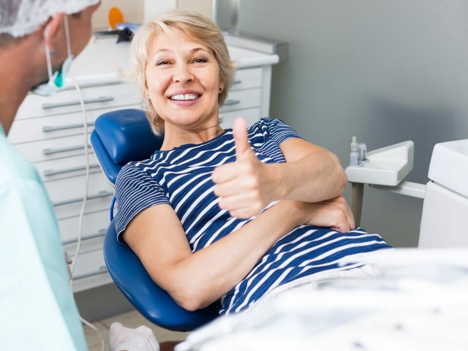 happy woman in dentist chair smiling with her thumb up