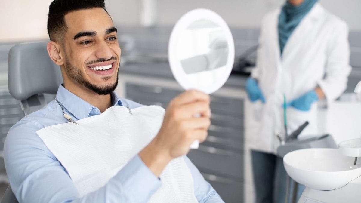 male looking at his teeth in a dental mirror