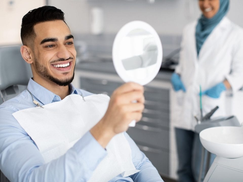male looking at his teeth in a dental mirror